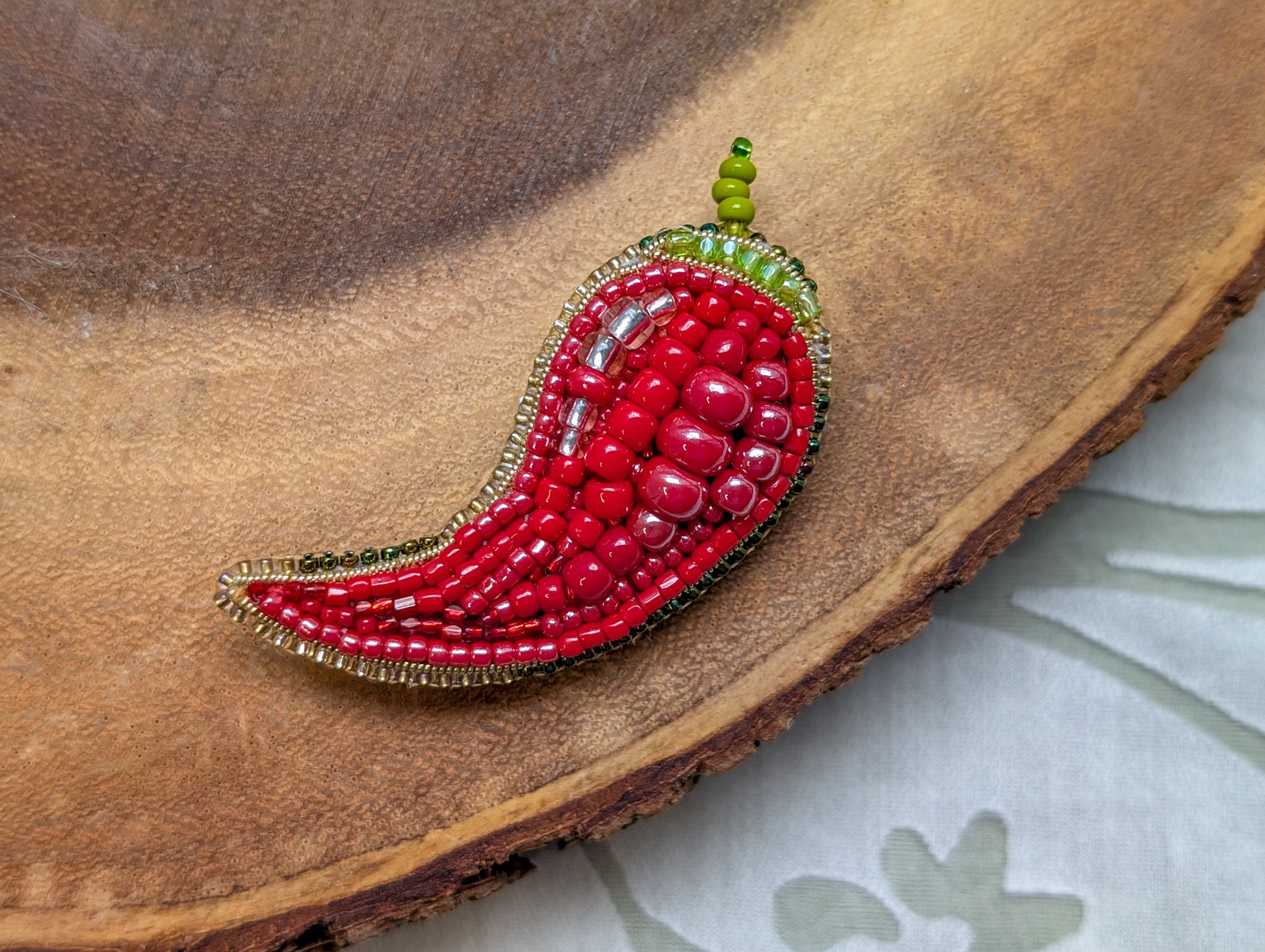 Beaded red chili pepper brooch on a wooden surface