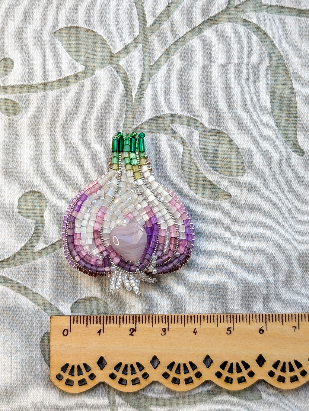 Beaded brooch with a ruler for scale on a decorative background