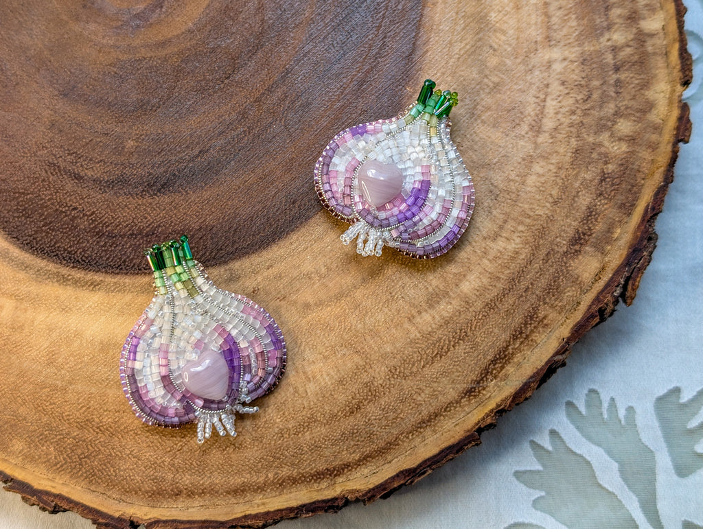 Two beaded garlic-shaped pins on a wooden surface

