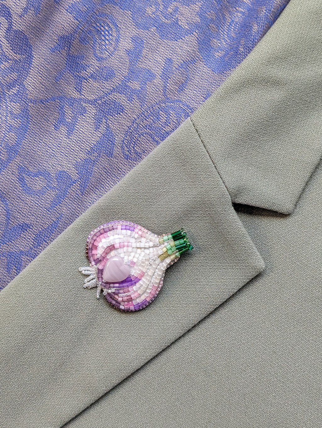 Beaded brooch on a gray fabric with a purple floral pattern

