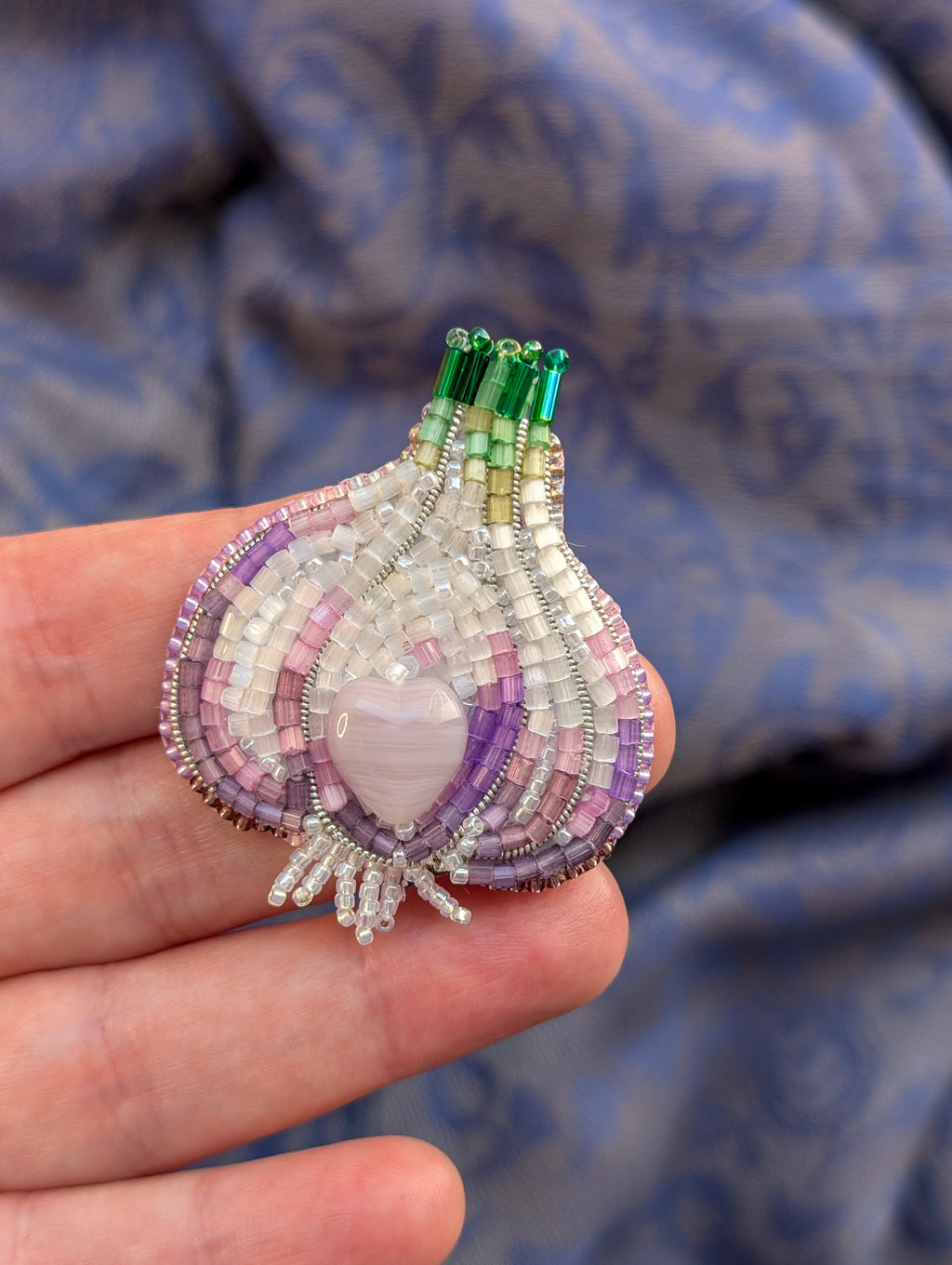 Beaded brooch with a heart-shaped center held in a hand against a blue fabric background

